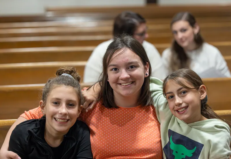 Three girls sitting together in the pews before a service.