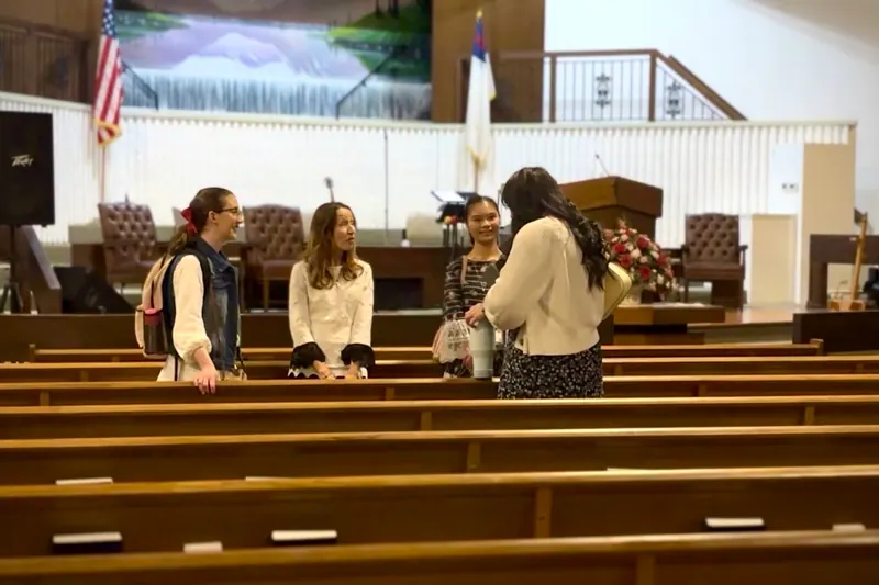 Four young women standing and talking together between the pews in the auditorium.