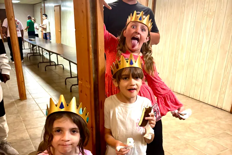 Three girls in gold paper crowns holding ice cream sandwiches in the church fellowship hall.