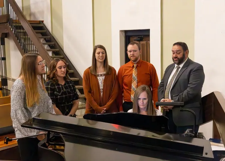 Pastor Paul Coyle with members of the church gathered around the grand piano before a service.