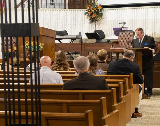 A preacher at the wooden pulpit during a service, with the congregation seated in the pews.